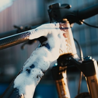 Bicicleta a ser lavada com espuma branca no quadro escuro e suspensão dourada em ambiente urbano