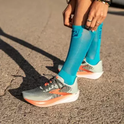 Ténis desportivos cinzentos com detalhes laranja e meias compressivas azuis claras