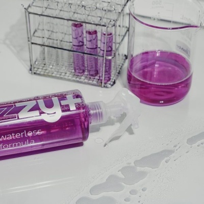 Frasco roxo de spray junto a tubos de ensaio e béquer com líquido roxo