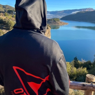 Pessoa de costas a usar hoodie preta com desenhos vermelhos e texto OTSO THINK SPORT, com paisagem natural e lago ao fundo