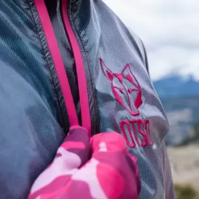 Peça de roupa cinzenta com logótipo rosa e mão com luva rosa segurando cordão