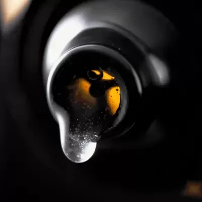 Garrafa de vidro escuro com líquido viscoso e gota transparente na abertura