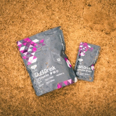 Produtos Glut5Drink em sacos cinzentos com padrões rosa e branco sobre terra