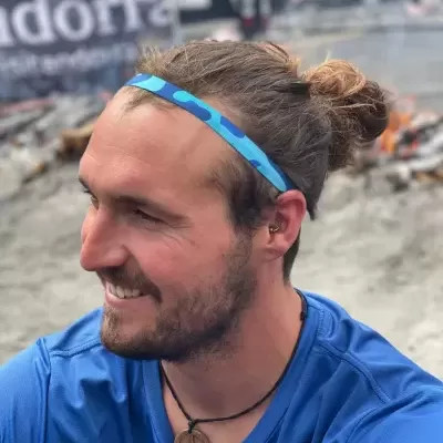 Homem com t-shirt azul e pulseira azul sentado em ambiente exterior com neve e fogo.