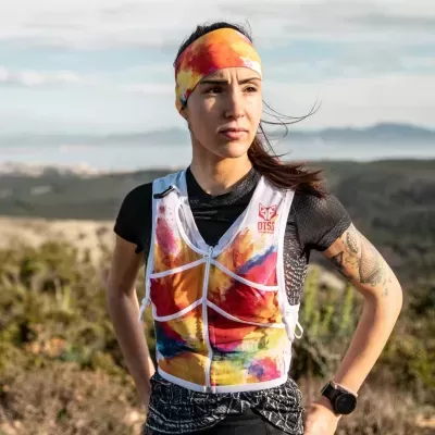 Mulher a usar faixa de cabeça e colete coloridos com padrão abstrato num cenário natural