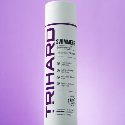Frasco branco de champô TRIHARD SWIMMERS com texto roxo e preto sobre fundo roxo e lilás