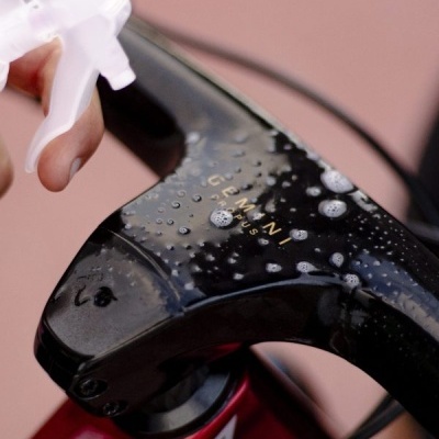 Peça preta de bicicleta com texto dourado sendo limpa com borrifador