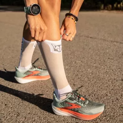 Meias de desporto brancas com logótipo cinzento e ténis verdes e laranja no pavimento