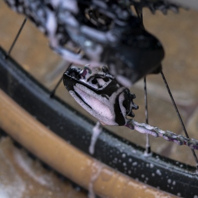 Roda traseira de bicicleta com espuma de limpeza cor-de-rosa no desviador e pneus castanhos em ambiente interior molhado