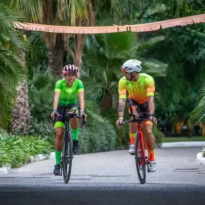 Dois ciclistas com roupa fluorescente numa estrada entre palmeiras.