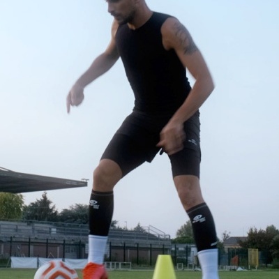 Atleta com roupa de treino preta e chuteiras vermelhas a praticar futebol ao ar livre