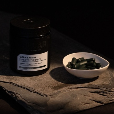 Frasco preto com cápsulas verdes num recipiente branco sobre pedra cinzenta