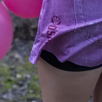 T-shirt cor-de-rosa com padrão tipo ganga e logótipo de raposa e texto PARTSO, com calções pretos, em ambiente exterior com balões rosa.