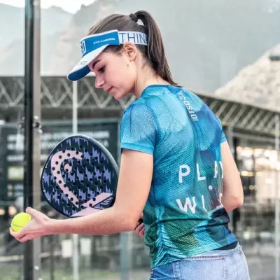 Mulher a jogar padel com t-shirt azul e verde, boné azul e raquete preta e roxa