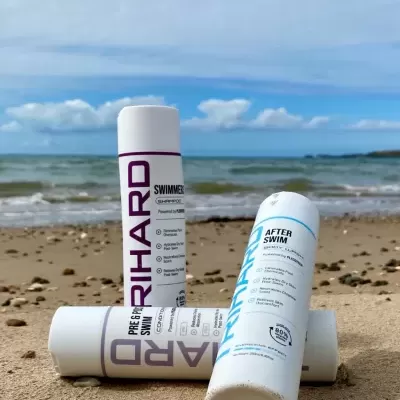 Três frascos brancos de champô para nadadores na areia da praia com mar ao fundo