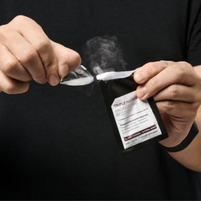 Mãos a abrir pacote preto com texto visível e vapor a sair