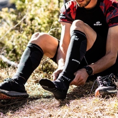 Meias desportivas pretas com texto BOOST usadas por homem sentado ao ar livre