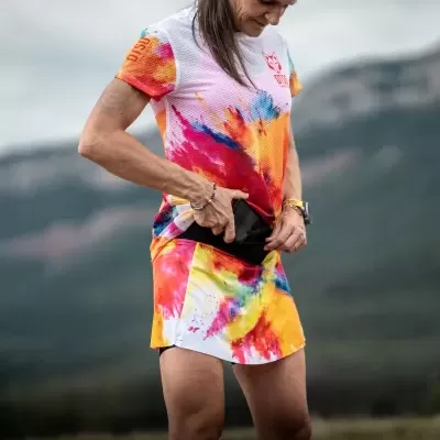 Mulher com roupa desportiva colorida padrão tie-dye, t-shirt e saia, ao ar livre em ambiente montanhoso