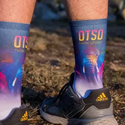 Pessoas com meias coloridas e ténis Adidas no chão de terra e relva