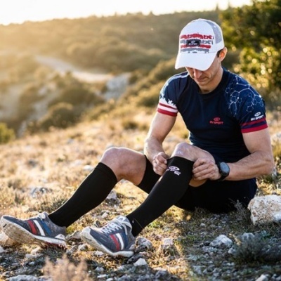 Homem sentado com roupa desportiva e ténis em terreno rochoso sob luz do sol
