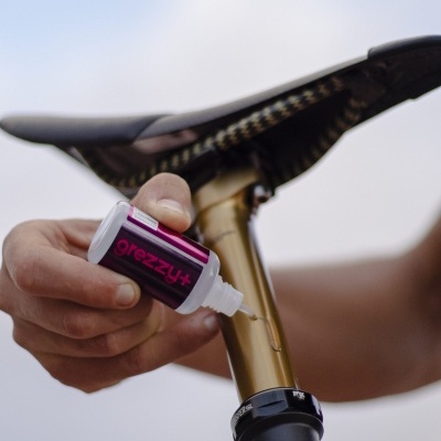 Frasco com líquido a ser aplicado num selim de bicicleta dourado e preto.