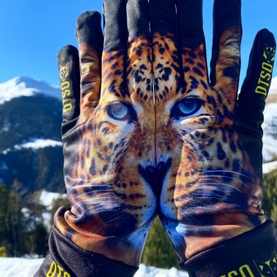 Luvas com estampa de onça-pintada seguradas contra cenário de neve e montanhas
