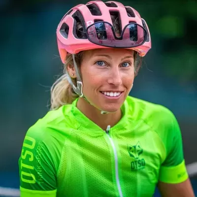 Mulher com capacete rosa e camisa verde neon de ciclismo sorrindo