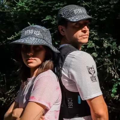 Duas pessoas com chapéu e boné cinza e preto com texto OTSO THINK SPORT em ambiente com folhagem verde