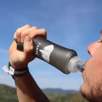 Garrafa de água dobrável preta com desenho geométrico e texto FANTE, usada ao ar livre.