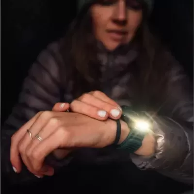 Pessoa com casaco cinza e gorro a usar relógio inteligente verde com luz acesa