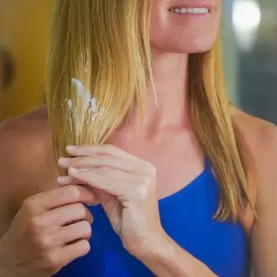 Mulher a aplicar creme no cabelo loiro, com camisola azul