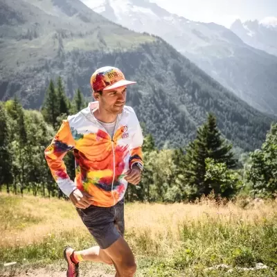 Homem a correr em trilho de montanha com casaco colorido e boné UTMB
