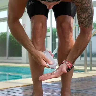 Homem com fato de banho preto aplicando creme protetor solar junto à piscina