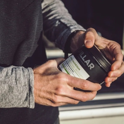 Pessoa segurando frasco preto com rótulo branco e texto parcial numa mão