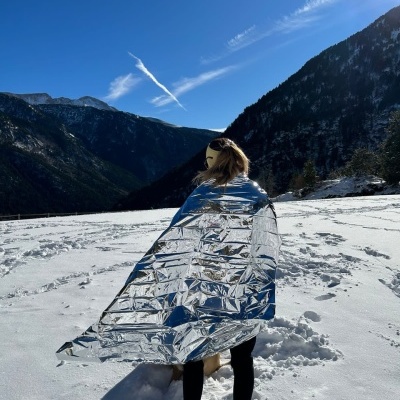 Pessoa envolvida com manta térmica prateada na neve, montanhas ao fundo