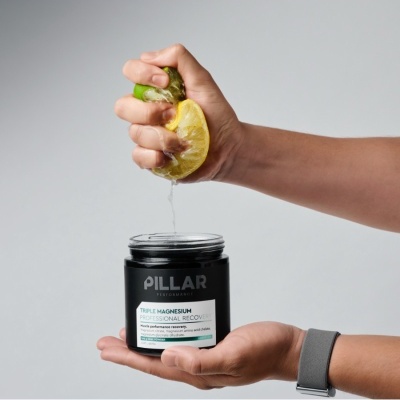 Frasco preto de suplemento PILLAR com rótulo branco em mãos, limão a ser espremido por cima