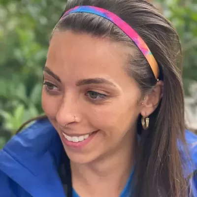 Faixa de cabelo elástica colorida usada por mulher com cabelo castanho e casaco azul em fundo de vegetação