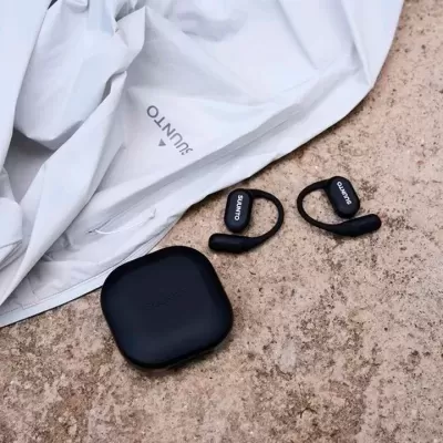 Auscultadores sem fios pretos com estojo preto e roupa branca com logo SUUNTO sobre superfície de pedra.