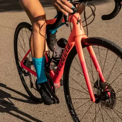 Bicicleta de estrada laranja Specialized com ciclista usando meias azuis e sapatos pretos