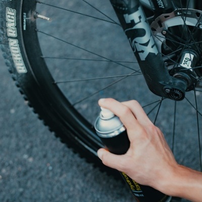 Roda de bicicleta preta com pneus CONTINENTAL REACTION RACE e suspensão FOX FACTORY com mão a usar spray