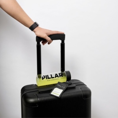 Mala preta de viagem com garrafa de perfume amarela PILLAR pendurada na alça