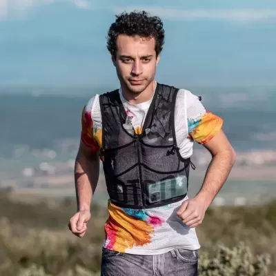 Homem a correr com mochila de hidratação preta e camiseta colorida ao ar livre