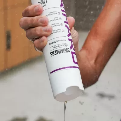 Mão a espremer shampoo líquido translúcido de embalagem branca cilíndrica para a mão