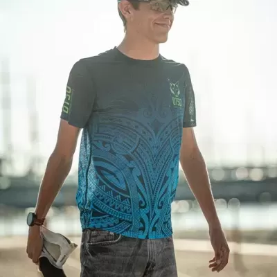 Homem a fazer alongamento na praia com t-shirt branca e azul e viseira azul escura