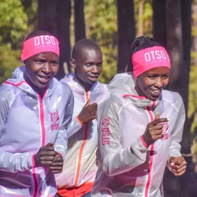 Três corredores com casacos transparentes e faixas rosas OTSO a correr em ambiente exterior