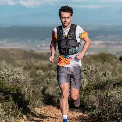 Homem a correr numa trilha com colete preto, t-shirt colorida e calções cinzentos