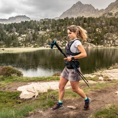 Mulher a correr em trilho natural junto a lago rodeado por montanhas e árvores