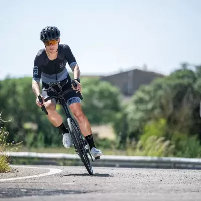 Ciclista de roupa preta e capacete a andar de bicicleta numa curva de estrada asfaltada