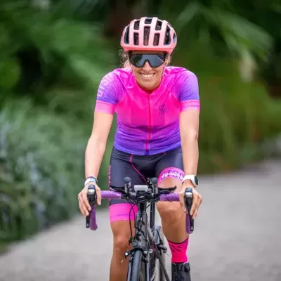 Mulher a andar de bicicleta com roupa de ciclismo rosa e roxa e capacete rosa