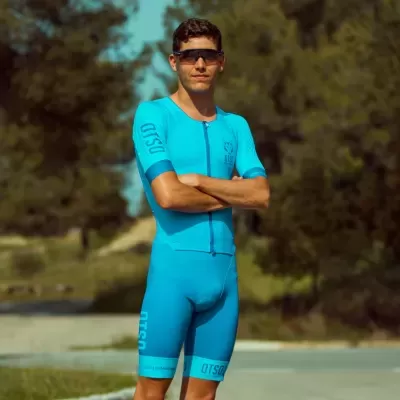 Homem com roupa de ciclismo azul claro e óculos escuros em ambiente ao ar livre